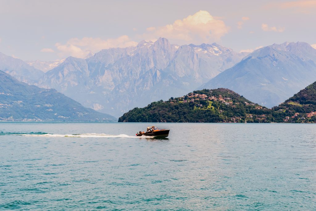 Wooden speedboat crossing Lake Como with mountains in the background
